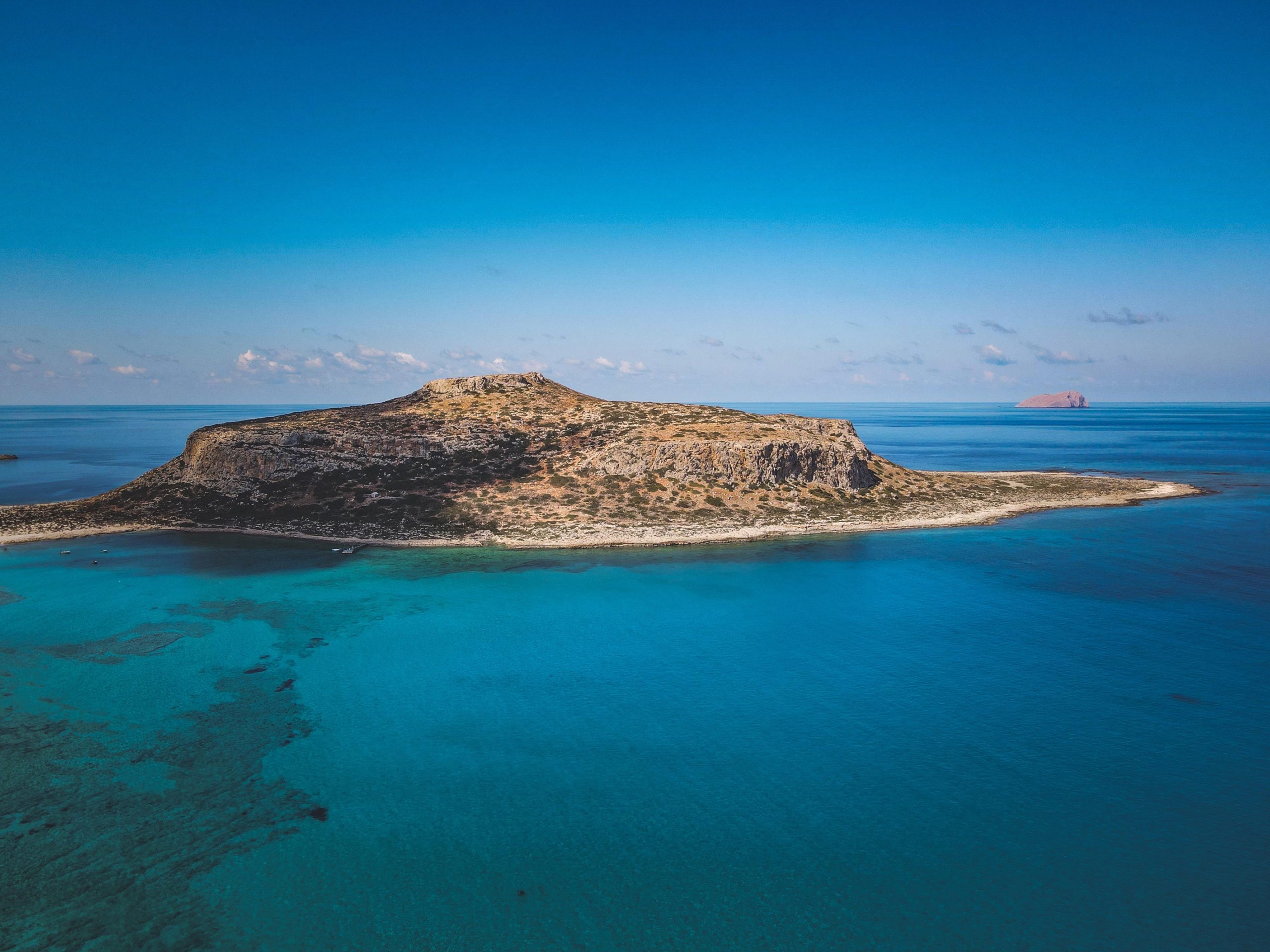 Breathtaking aerial photo of an isolated rocky island surrounded by the bright blue ocean waters.