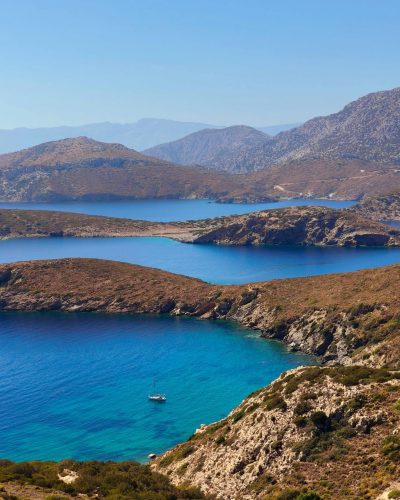 Aerial view of a serene coastal landscape with turquoise waters and rolling hills under a clear blue sky.